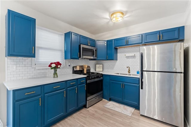 kitchen featuring stainless steel appliances, backsplash, sink, blue cabinets, and light hardwood / wood-style flooring