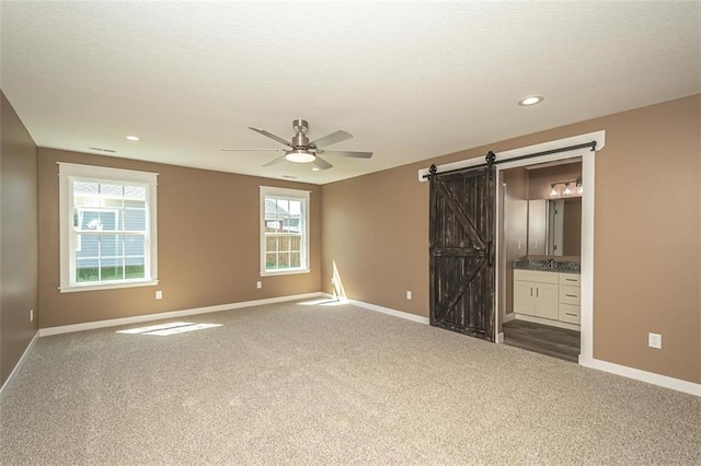 unfurnished bedroom with dark carpet, baseboards, and a barn door