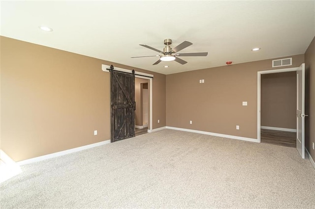 unfurnished room with a ceiling fan, visible vents, a barn door, light carpet, and baseboards