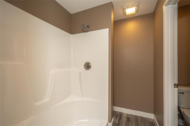 full bathroom featuring toilet, a shower, wood finished floors, and baseboards