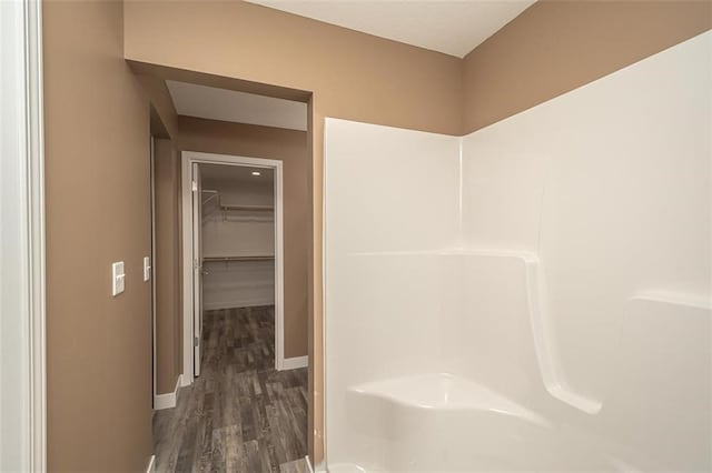 full bathroom with a shower, wood finished floors, baseboards, and a spacious closet
