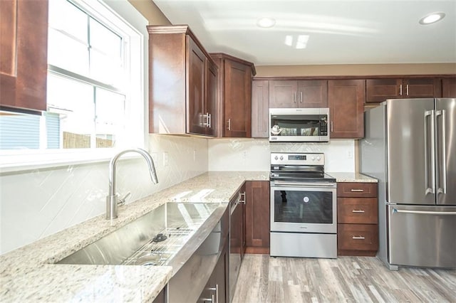 kitchen with light wood-style flooring, a sink, appliances with stainless steel finishes, light stone countertops, and decorative backsplash