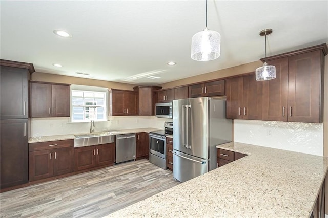 kitchen featuring light stone counters, light wood-style flooring, decorative light fixtures, stainless steel appliances, and a sink