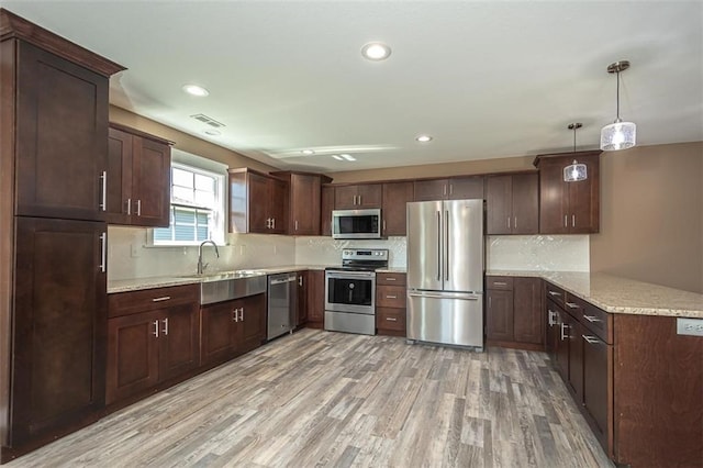 kitchen with light wood-style flooring, a peninsula, tasteful backsplash, a sink, and stainless steel appliances