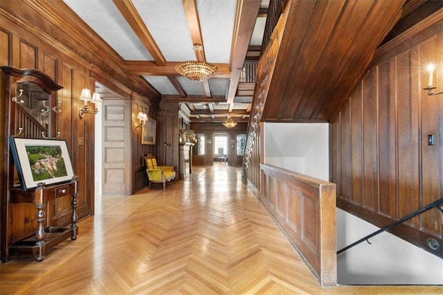 hall featuring beamed ceiling, light parquet flooring, wood walls, and an inviting chandelier