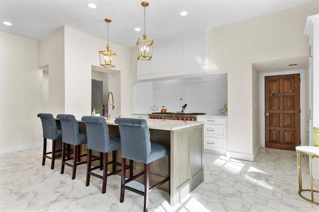 kitchen featuring backsplash, white cabinets, an island with sink, and decorative light fixtures