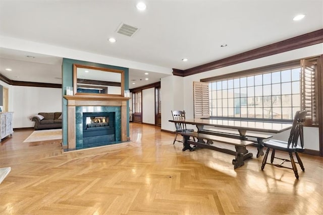 dining room featuring crown molding, a fireplace, and light parquet flooring