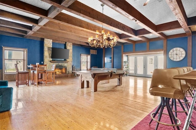 rec room with beam ceiling, a fireplace, french doors, and light hardwood / wood-style flooring