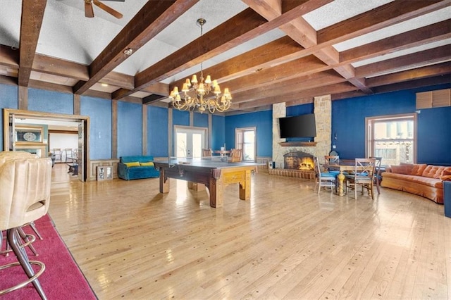 playroom featuring beamed ceiling, french doors, light hardwood / wood-style floors, and a stone fireplace