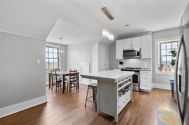 kitchen with a center island, stainless steel appliances, pendant lighting, wood-type flooring, and white cabinets