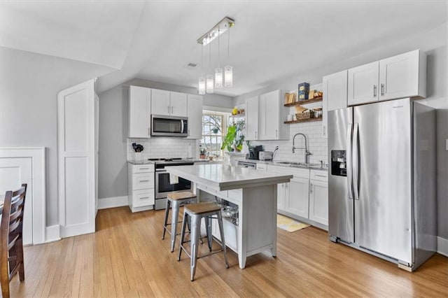 kitchen with appliances with stainless steel finishes, white cabinetry, a kitchen island, and sink