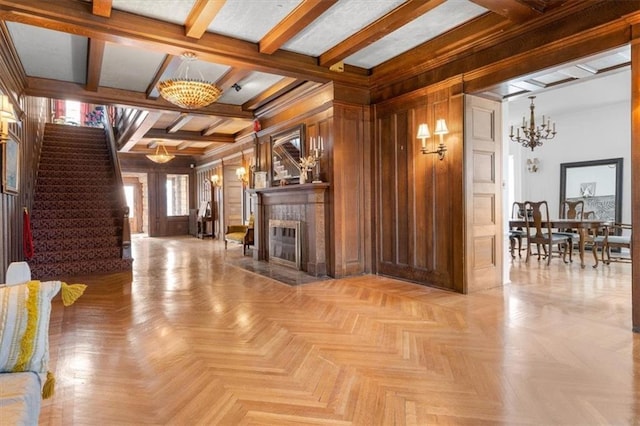 living room with a notable chandelier, wood walls, a tile fireplace, beamed ceiling, and stairs