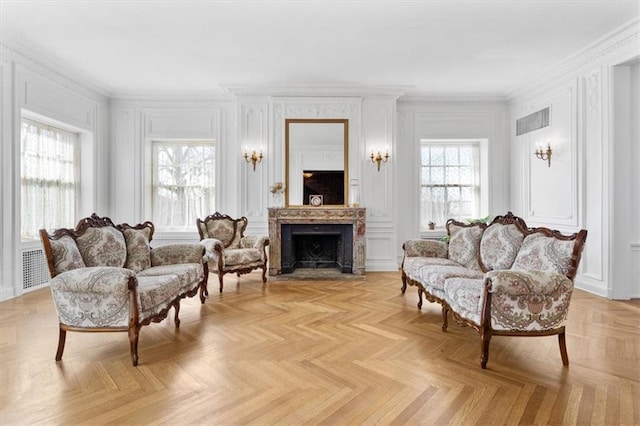 living area with ornamental molding, a fireplace with flush hearth, visible vents, and a decorative wall