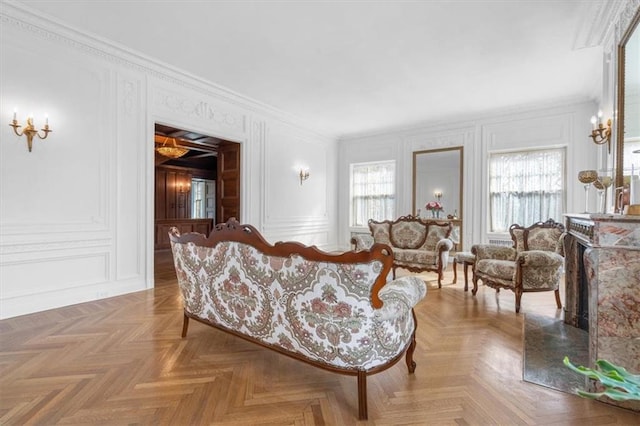 living room with a healthy amount of sunlight, a decorative wall, crown molding, and a high end fireplace