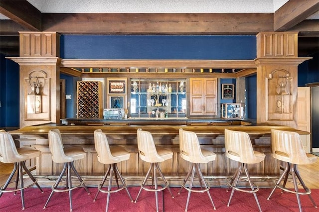 bar with a bar, wood finished floors, and beam ceiling