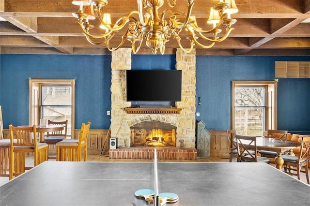 recreation room with beam ceiling, coffered ceiling, a notable chandelier, and a stone fireplace