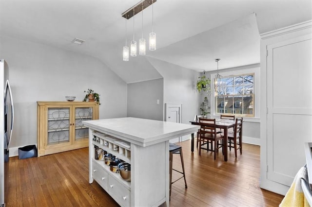 kitchen featuring visible vents, wood-type flooring, a kitchen island, a breakfast bar area, and vaulted ceiling