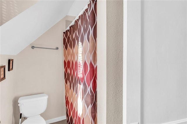 bathroom featuring toilet, a shower with shower curtain, baseboards, and lofted ceiling