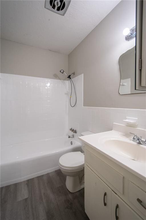 full bathroom featuring hardwood / wood-style floors, shower / washtub combination, vanity, toilet, and tile walls