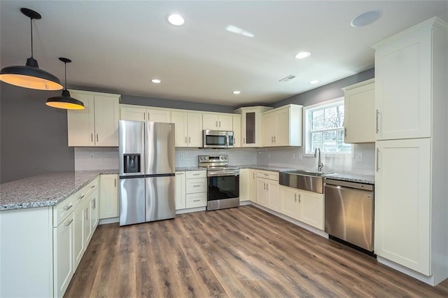 kitchen with appliances with stainless steel finishes, dark hardwood / wood-style flooring, light stone counters, sink, and decorative light fixtures