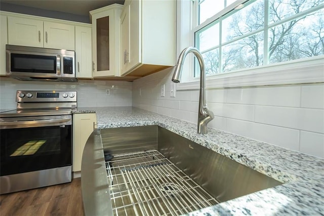 interior details featuring backsplash, light stone countertops, dark hardwood / wood-style flooring, white cabinetry, and stainless steel appliances