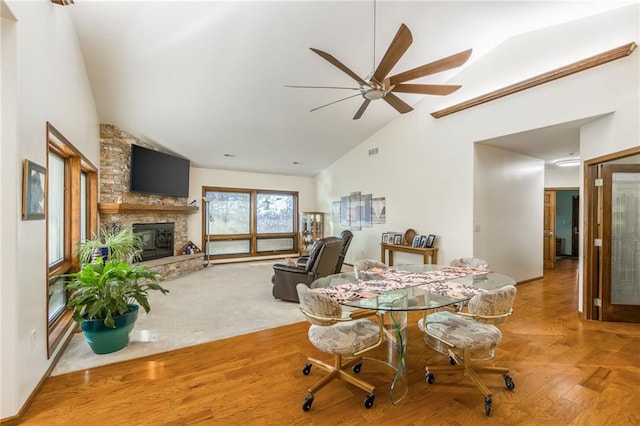 dining room featuring ceiling fan, a large fireplace, wood-type flooring, and high vaulted ceiling