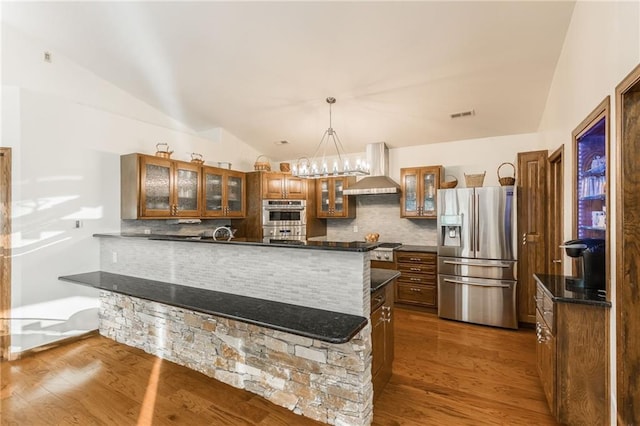 kitchen with hardwood / wood-style flooring, wall chimney range hood, stainless steel appliances, and vaulted ceiling