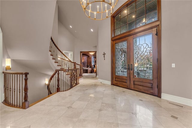 foyer entrance featuring a towering ceiling, french doors, and a notable chandelier