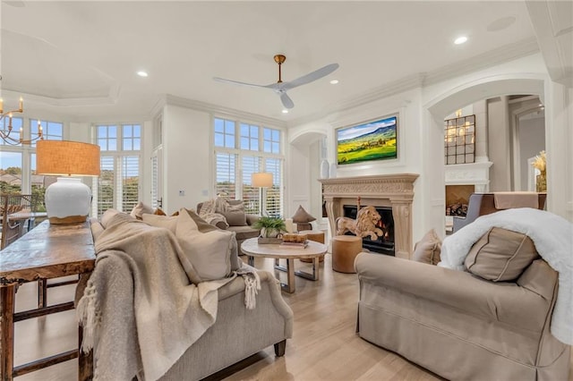 living room featuring ceiling fan with notable chandelier, a healthy amount of sunlight, light wood-type flooring, and ornamental molding