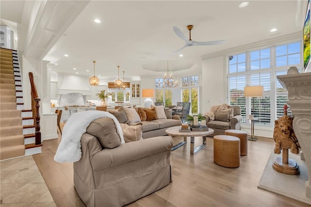 living room with light hardwood / wood-style floors, ceiling fan with notable chandelier, and ornamental molding