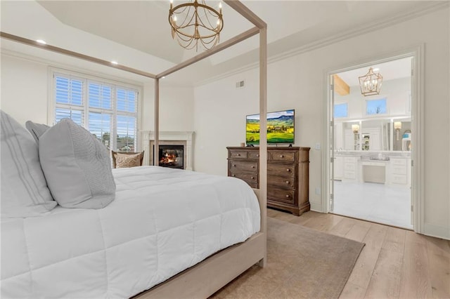 bedroom featuring light hardwood / wood-style floors, ornamental molding, an inviting chandelier, a tray ceiling, and connected bathroom