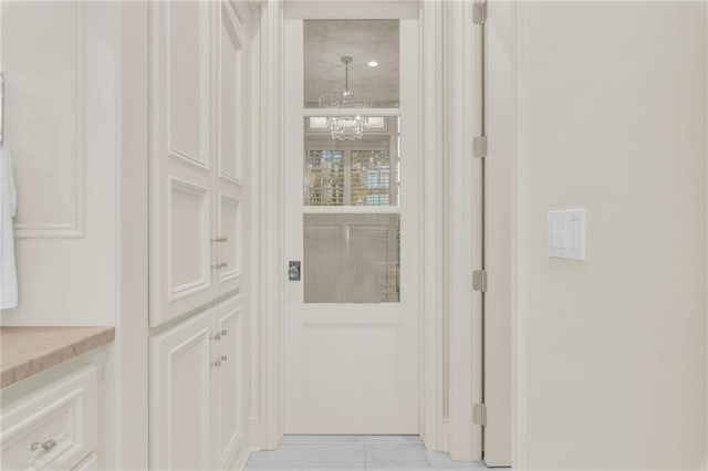 hall with light tile patterned flooring and an inviting chandelier