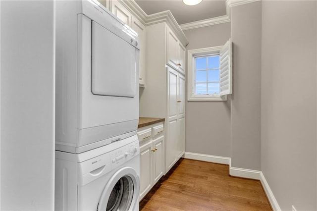 washroom with cabinets, stacked washing maching and dryer, light hardwood / wood-style floors, and ornamental molding