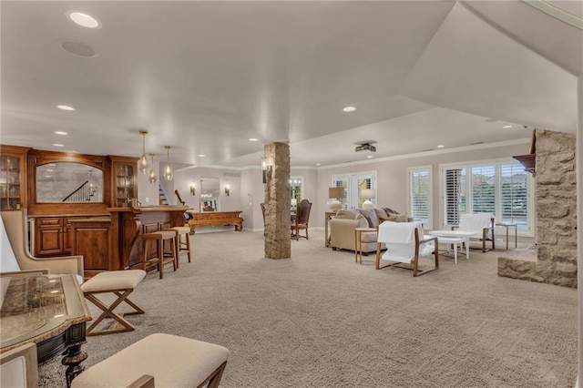 carpeted living room featuring bar area, ornate columns, and crown molding