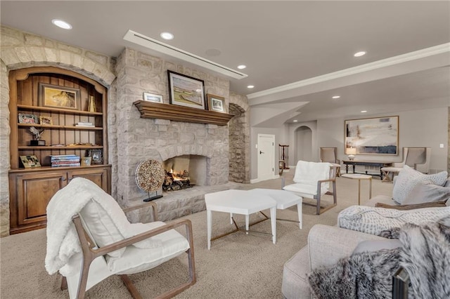 carpeted living room featuring a stone fireplace, crown molding, and built in shelves