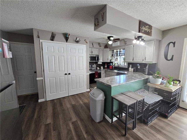 kitchen with appliances with stainless steel finishes, dark hardwood / wood-style flooring, white cabinets, kitchen peninsula, and ceiling fan