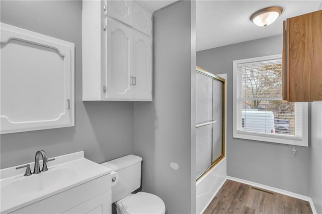 full bathroom featuring hardwood / wood-style flooring, bath / shower combo with glass door, vanity, and toilet