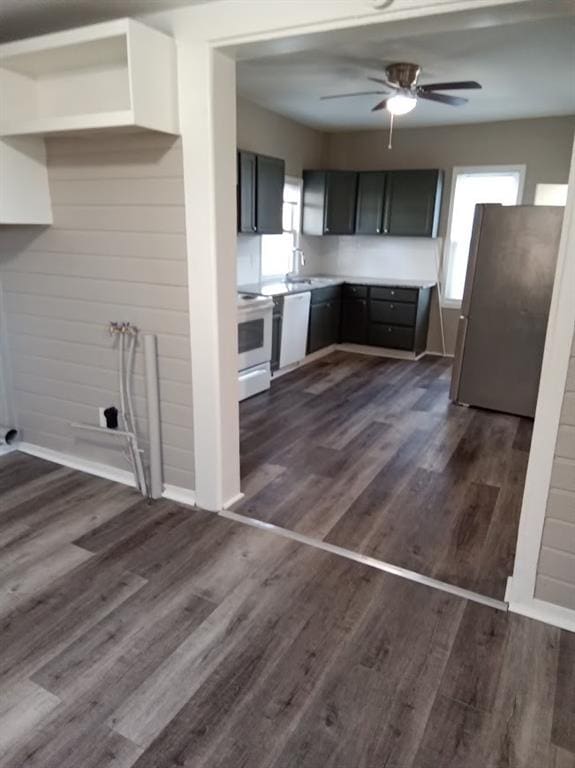 kitchen with dark wood-type flooring, wood walls, sink, ceiling fan, and white appliances