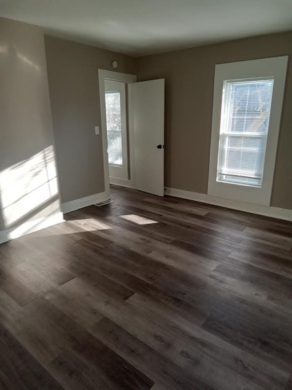 empty room featuring plenty of natural light and dark wood-type flooring