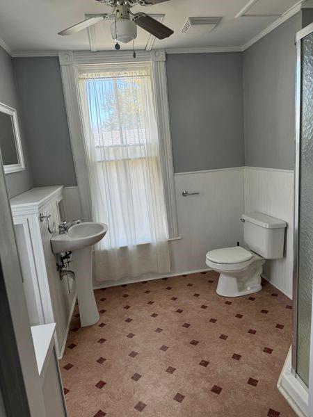 bathroom with crown molding, sink, toilet, ceiling fan, and a shower with shower door