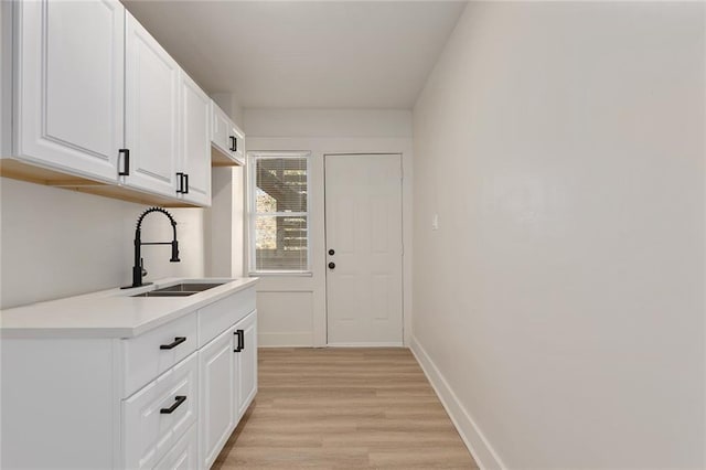 interior space with white cabinetry, sink, and light hardwood / wood-style flooring