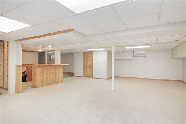 basement with bar area, light colored carpet, and a paneled ceiling