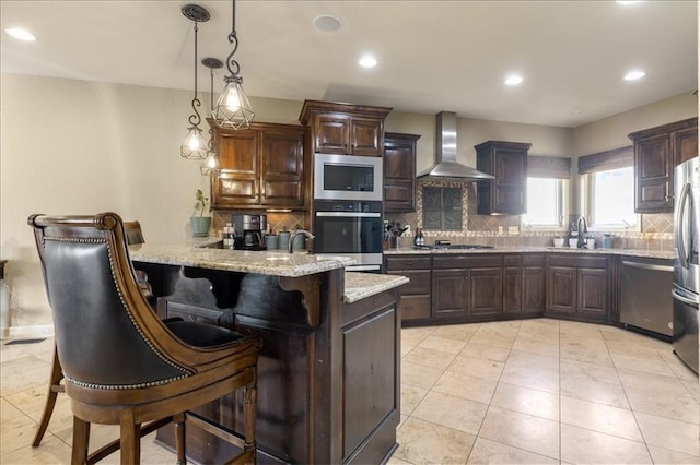 kitchen with stainless steel appliances, wall chimney range hood, dark brown cabinets, a kitchen breakfast bar, and kitchen peninsula