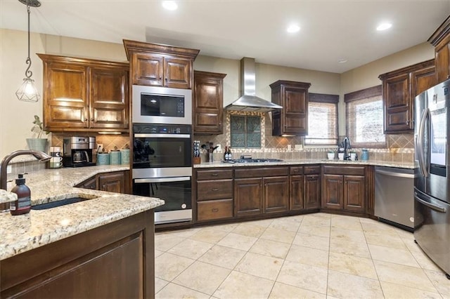 kitchen with appliances with stainless steel finishes, hanging light fixtures, sink, and wall chimney range hood