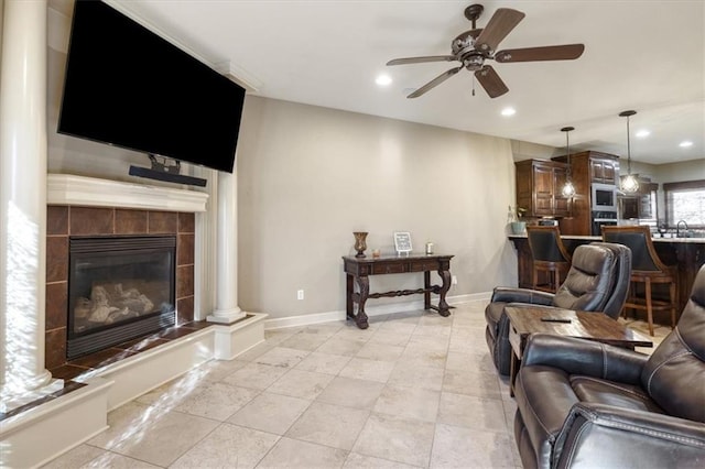 living room with a tiled fireplace, ceiling fan, sink, and decorative columns