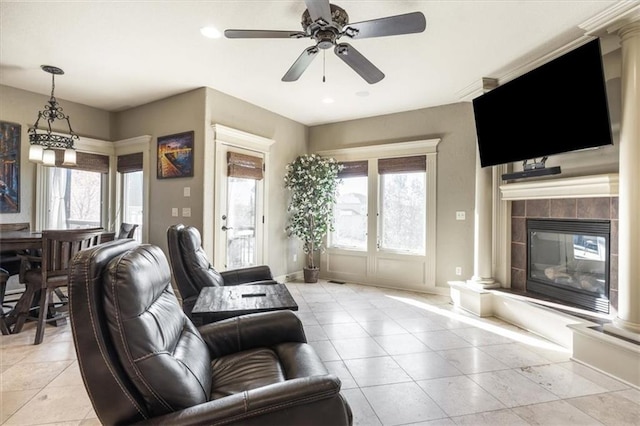 tiled living room with a wealth of natural light, ceiling fan, a tile fireplace, and decorative columns