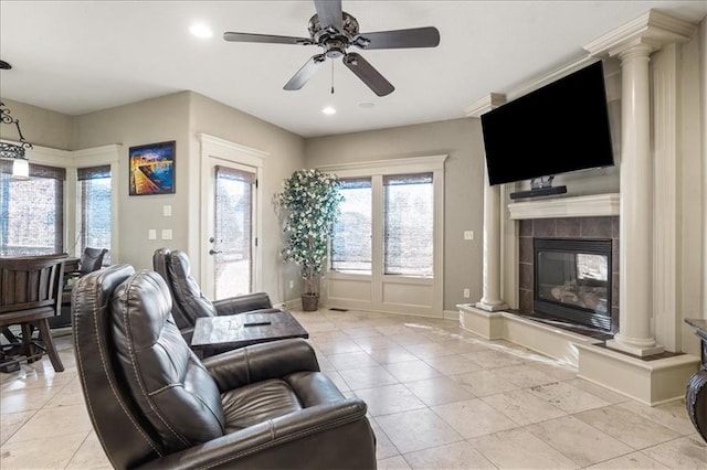 tiled living room with ceiling fan, a tile fireplace, and ornate columns