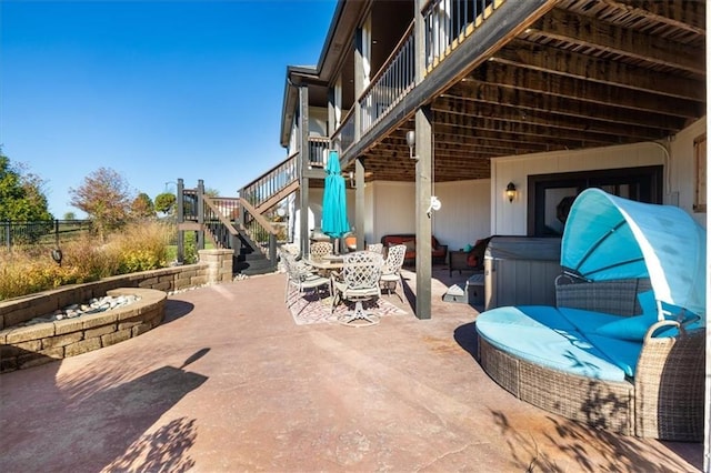 view of patio with a hot tub, a fire pit, and a balcony