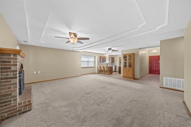 unfurnished living room featuring a fireplace, a textured ceiling, a raised ceiling, light colored carpet, and ceiling fan