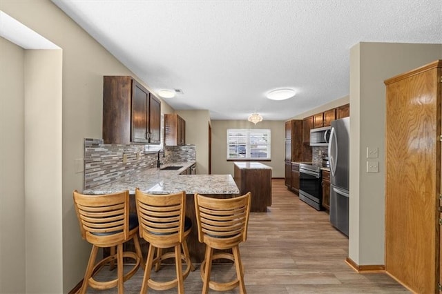 kitchen featuring a kitchen bar, stainless steel appliances, kitchen peninsula, sink, and light hardwood / wood-style flooring